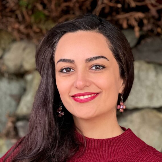 A picture of Elmira Fakhr wearing a bright red sweater and with bright red lipstick